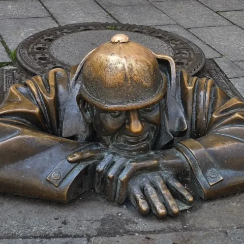 Bronzen beeld Čumil dat uit een putdeksel kijkt in Bratislava
