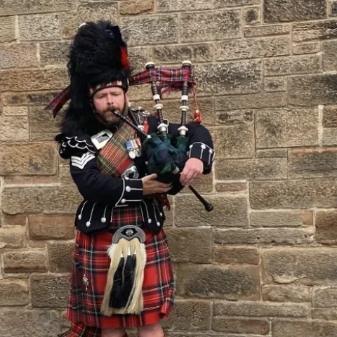 Doedelzakspeler in kilt voor een stenen muur